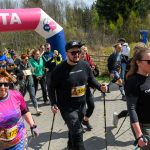 DSC_6076 Grupa osób idzie z kijkami do nordic walking pod różowym napisem META. Tło stanowi zielony las i niebo. Uczestnicy noszą kolorowe ubrania.