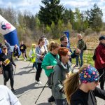DSC_6080 Grupa ludzi uczestniczy w rajdzie nordic walking, mija kolorowy balon startowy. Ciepłe ubrania sugerują chłodny dzień. W tle widać las.