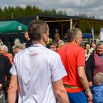 DSC_6150 Grupa ludzi na świeżym powietrzu, słońce, zielone tło; centralnie kobieta w czarnej koszulce z białym nadrukiem, dwóch mężczyzn w sportowych koszulkach.
