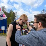 DSC_6198 Osoba nakłada medal biegaczowi przy mecie w plenerze. W tle widoczne są drzewa i fragment różowego balonu. Na podświetlaczu widnieje czas 00:29:35.