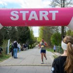 DSC_6271 Biegacz przekracza linię startu, różowy balon z napisem START. W tle las i kibice, niebo częściowo zachmurzone.