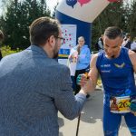 DSC_6288 Na zdjęciu mężczyzna w niebieskim stroju sportowym na zawodach. W tle zielone drzewa i ludzie na chodniku. Scena na świeżym powietrzu.